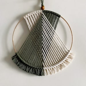 May include: A green and white macrame wall hanging with a gold hoop and fringe. The macrame is in a geometric pattern.