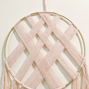 May include: A pink yarn dream catcher with a gold metal hoop and fringe. The yarn is woven in a criss-cross pattern.