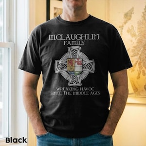 May include: A black short-sleeve t-shirt featuring a white Celtic cross graphic with a central shield emblem. The text reads MCLAUGHLIN FAMILY above the cross and WREAKING HAVOC SINCE THE MIDDLE AGES below the cross in a white serif font.