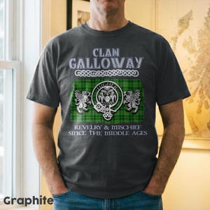 May include: Graphite gray t-shirt featuring the text "Clan Galloway" above a green and black plaid design with a crest and the words "Revelry & Mischief Since The Middle Ages."