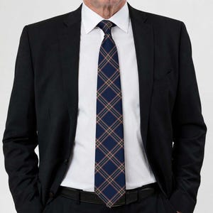 May include: A navy blue necktie featuring a diagonal plaid pattern with thin intersecting lines in light orange and white. The tie is worn with a crisp white collared dress shirt and a tailored black suit jacket, creating a formal ensemble.