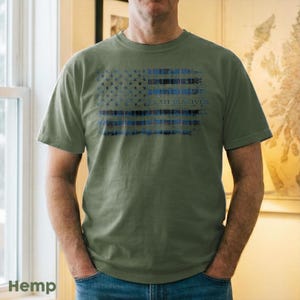 May include: Olive green t-shirt with a distressed American flag design in blue and black. The shirt has the text "CLAIR REACTIV" across the flag. The word "Hemp" is printed at the bottom left corner.