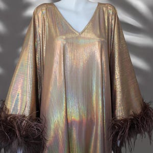 May include: A long, gold metallic dress with iridescent shimmer. The dress has a V-neck and long sleeves with brown feather trim.