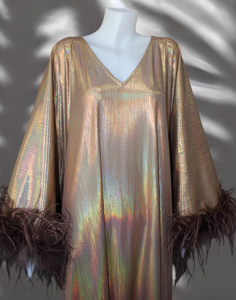 May include: A long, gold metallic dress with iridescent shimmer. The dress has a V-neck and long sleeves with brown feather trim.