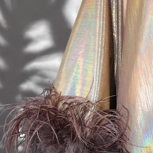 May include: A gold iridescent fabric with a brown feather trim. The fabric has a subtle shimmer and a textured surface.
