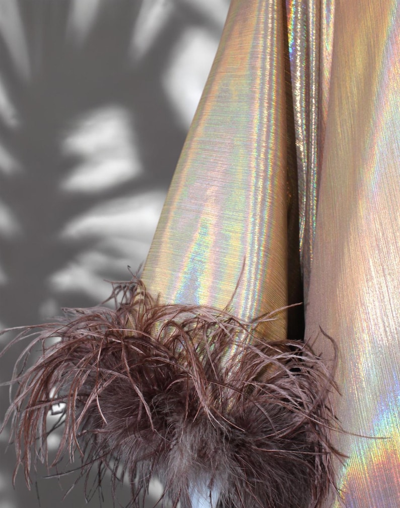 May include: A gold iridescent fabric with a brown feather trim. The fabric has a subtle shimmer and a textured surface.