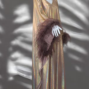 May include: A long, iridescent gold dress with a V-neckline and long sleeves. The sleeves are trimmed with brown feathers.
