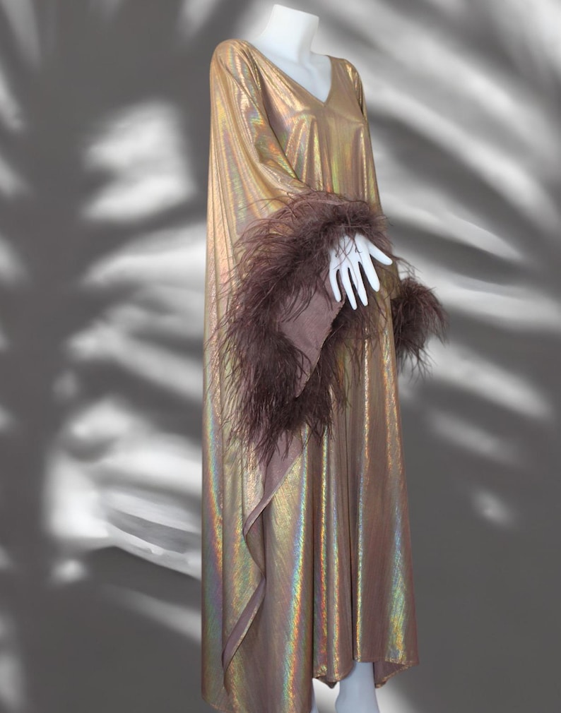 May include: A long, iridescent gold dress with a V-neckline and long sleeves. The sleeves are trimmed with brown feathers.