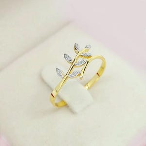 Könnte beinhalten: Ein goldener Ring mit einem zarten Blattdesign, das mit kleinen, klaren Steinen besetzt ist.