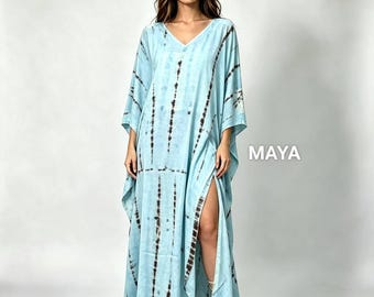May include: A floor-length light blue kaftan dress featuring a dark brown vertical tie-dye pattern, a V-neckline, wide sleeves, and a high side slit. The word MAYA is printed in white letters on the right side of the garment.