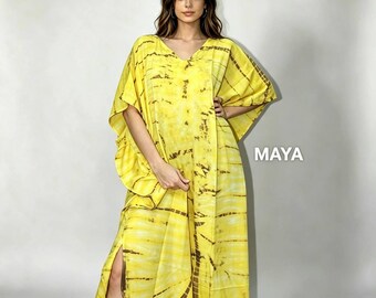 May include: A floor-length yellow kaftan dress featuring a dark brown tie-dye pattern with radiating lines. The garment has a V-neckline, wide kimono-style sleeves, and a high side slit on the right leg. The word MAYA is printed in white text.