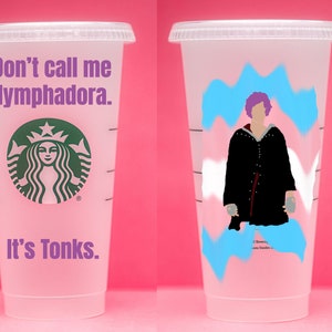 May include: A white reusable cup with a purple and blue design. The cup has a black silhouette of a person with purple hair wearing a black robe. The text "Don't call me Nymphadora. It's Tonks." is on the other side of the cup.