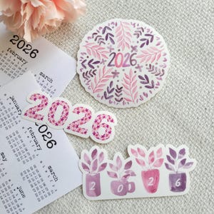 May include: A selection of stickers and calendar pages with a floral theme. The stickers display the year "2026" in different styles, including floral patterns and potted plants. The colour scheme includes shades of pink and purple.