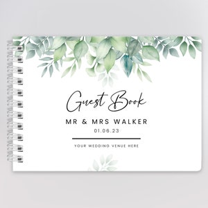 May include: White guest book with a green watercolour floral design. The text on the cover reads "Guest Book", "Mr & Mrs Walker", "01.06.23", and "Your Wedding Venue Here".