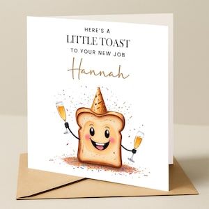 May include: A white card with a cartoon illustration of a slice of toast wearing a party hat and holding two glasses of champagne. The text on the card reads "Here's a little toast to your new job Hannah".