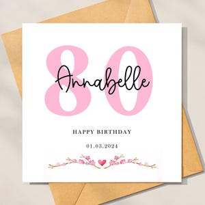 Può includere: Biglietto di auguri di compleanno rosa e bianco con il numero 80 e il nome Annabelle in corsivo nero. Il biglietto ha un design floreale con fiori rosa e un piccolo cuore rosso. Il testo "Buon compleanno" e la data "01.03.2024" sono stampati sotto il numero.