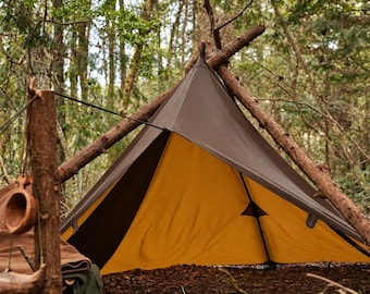 May include: A pyramid-shaped tent featuring a dark brown exterior and a bright yellow interior. The tent is supported by a wooden frame structure made of branches and is positioned in a wooded area with a wooden cup hanging nearby.