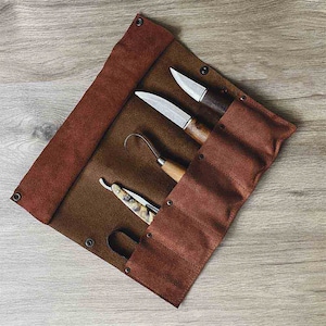 May include: A brown leather roll-up case with five slots for holding tools. The case is open and shows a small knife, a larger knife, a carving tool, and a straight razor.