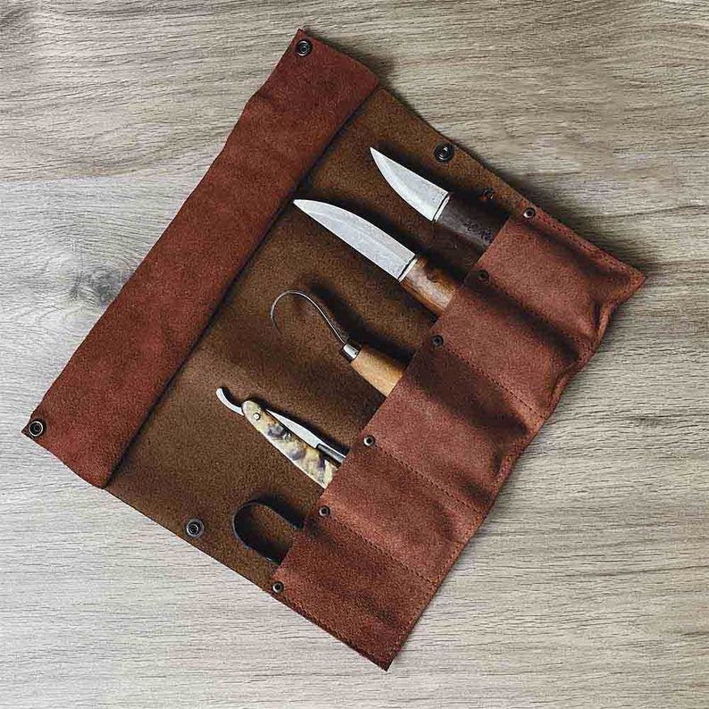 May include: A brown leather roll-up case with five slots for holding tools. The case is open and shows a small knife, a larger knife, a carving tool, and a straight razor.
