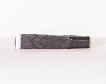 Può includere: Un cuneo spaccatutto in metallo grigio scuro con un motivo a zig-zag sulla parte superiore. Il cuneo ha un bordo piatto e lucido color argento e un'estremità sfaccettata. Progettato per spaccare la legna.
