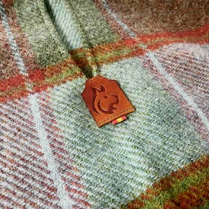 May include: A brown leather patch with a stylized animal design, attached to a plaid fabric with green, white, and orange stripes.