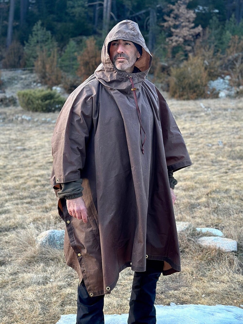 May include: A brown hooded poncho with a drawstring closure and brass eyelets. The poncho is made of a water-resistant material and has a long, flowing design.