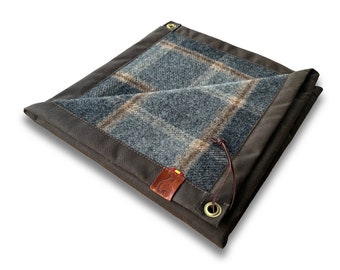 May include: A brown canvas blanket with a plaid wool lining. The blanket has a leather patch with a logo and a leather strap with a brass grommet.