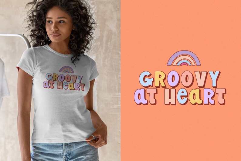 May include: White t-shirt featuring the text "GROOVY at HEART" in a colourful, retro font, with a rainbow design. The shirt is worn by a person. The background is a light orange colour.