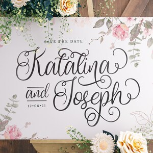 Pu&ograve; includere: Un cartello bianco "Save the Date" con disegni floreali ad acquerello. Il testo recita "Save the Date" e "Catalina e Joseph" con la data "12.08.21" sotto.