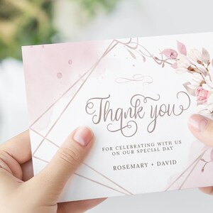 Pu&ograve; includere: Un biglietto di ringraziamento rosa e bianco con un design floreale e accenti geometrici dorati. Il biglietto recita "Grazie" e "Per aver festeggiato con noi il nostro giorno speciale. Rosemary + David."