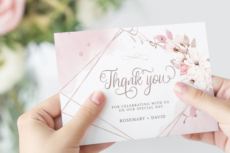 Pu&ograve; includere: Un biglietto di ringraziamento rosa e bianco con un design floreale e accenti geometrici dorati. Il biglietto recita "Grazie" e "Per aver festeggiato con noi il nostro giorno speciale. Rosemary + David."