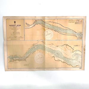May include: Vintage map of the Saguenay River, featuring detailed nautical charts. The map has a beige background with green and brown details, including compass roses. The title "SAGUENAY RIVER" is visible at the top.