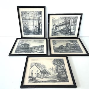May include: Five framed black and white landscape prints. The prints depict various scenes, including a lake with trees, a building with a tower, and a street with houses. The frames are black.
