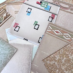 May include: A collection of vintage wallpaper samples in various patterns and colors. The samples include geometric designs, floral motifs, and textured surfaces. Colors range from beige and cream to green and brown.
