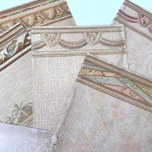 May include: Assortment of wallpaper border samples with various decorative designs. The borders feature ornate patterns in beige, brown, and pastel colors. Some samples have floral and geometric motifs, while others showcase textured surfaces.