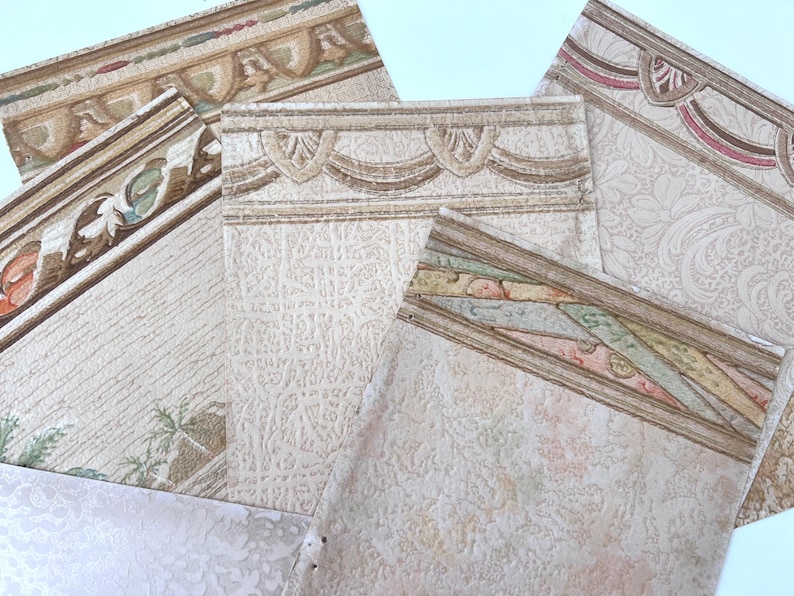 May include: Assortment of wallpaper border samples with various decorative designs. The borders feature ornate patterns in beige, brown, and pastel colors. Some samples have floral and geometric motifs, while others showcase textured surfaces.