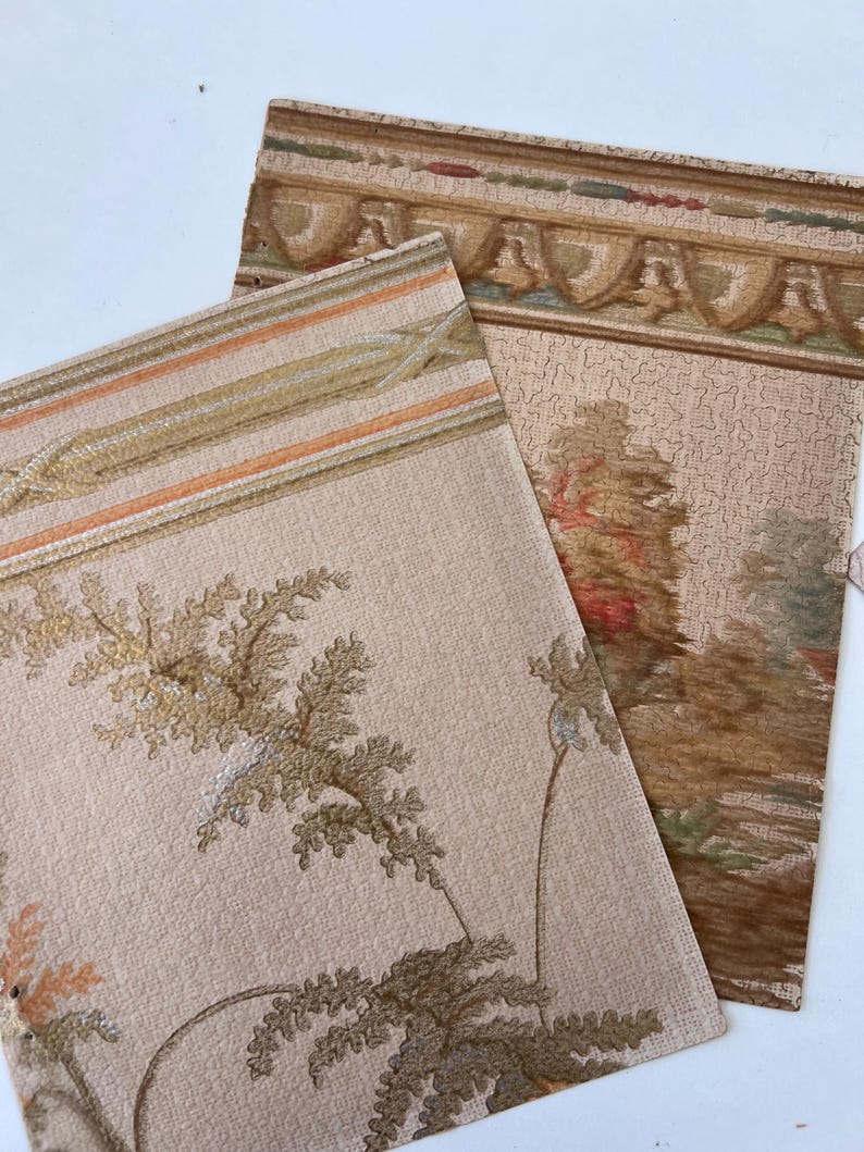 May include: Two pieces of vintage wallpaper with a beige background. One piece features a floral design with brown and gold accents. The other piece has a decorative border with a landscape scene in shades of brown, green, and red.