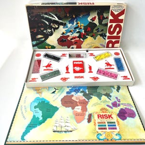 May include: A vintage RISK board game with a world map game board. The box lid features a cannon and a map. Inside, there are game pieces in red, yellow, blue, and green. The game board shows continents and oceans.