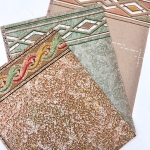 May include: A collection of vintage wallpaper samples. The samples feature various patterns, including geometric diamond shapes, wavy lines, and textured backgrounds in shades of brown, green, and beige. The edges have decorative borders.
