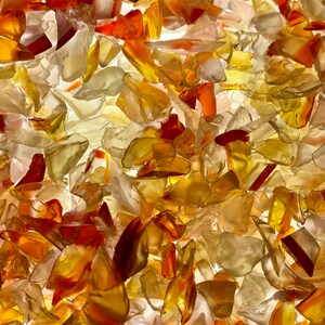 May include: Abstract image of a mosaic of translucent glass pieces in shades of amber, orange, and white. The irregular shapes are illuminated from behind, creating a glowing effect. The overall texture is dense and layered.