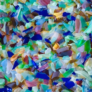 May include: Close-up of a collection of colorful sea glass pieces. The fragments vary in size and shape, with colors including blue, green, pink, and clear. The sea glass has a frosted appearance.
