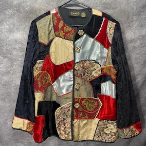 Puede incluir: Una chaqueta de manga larga con un diseño de patchwork que combina paneles de terciopelo negro, terciopelo rojo, brocado dorado y satén plateado. La chaqueta tiene cuello redondo, cierre frontal con cinco botones redondos y una etiqueta negra.