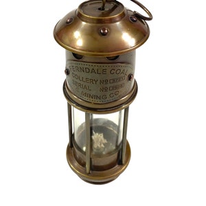 May include: Brass miner's lamp with a glass lens and a handle. The lamp has a label that reads "Ferndale Coal Colliery No 3721 Serial No 2908 & Mining Co."