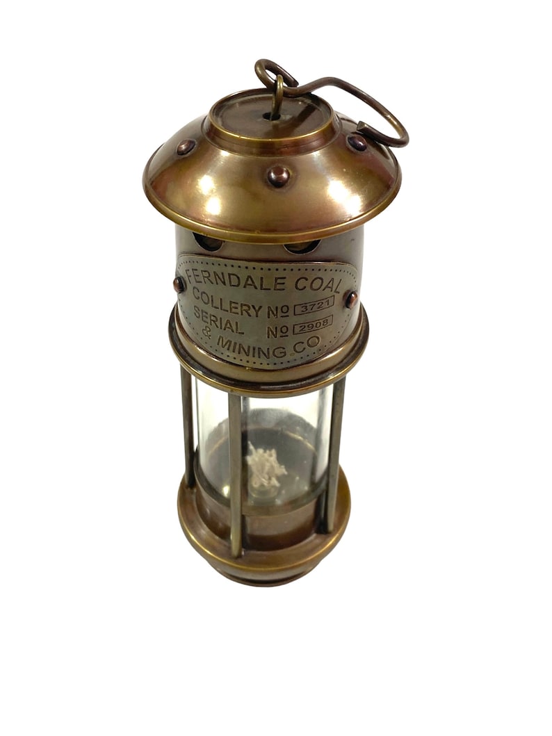May include: Brass miner's lamp with a glass lens and a handle. The lamp has a label that reads "Ferndale Coal Colliery No 3721 Serial No 2908 & Mining Co."
