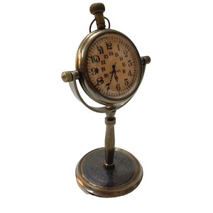 May include: A brass desk clock with a round face and Roman numeral markings. The clock has a stand with a round base and a decorative design.