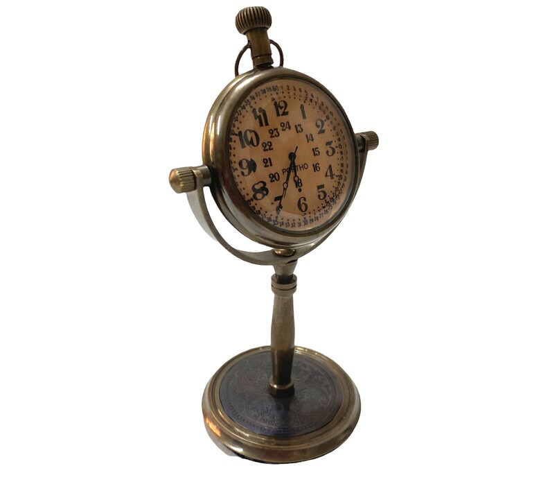 May include: A brass desk clock with a round face and Roman numeral markings. The clock has a stand with a round base and a decorative design.