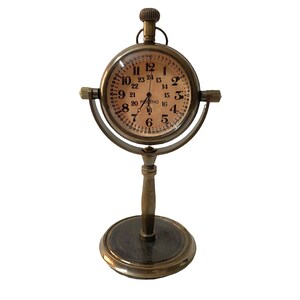 May include: A brass desk clock with a round face and a stand. The clock face has black Roman numerals and a 24-hour time scale.