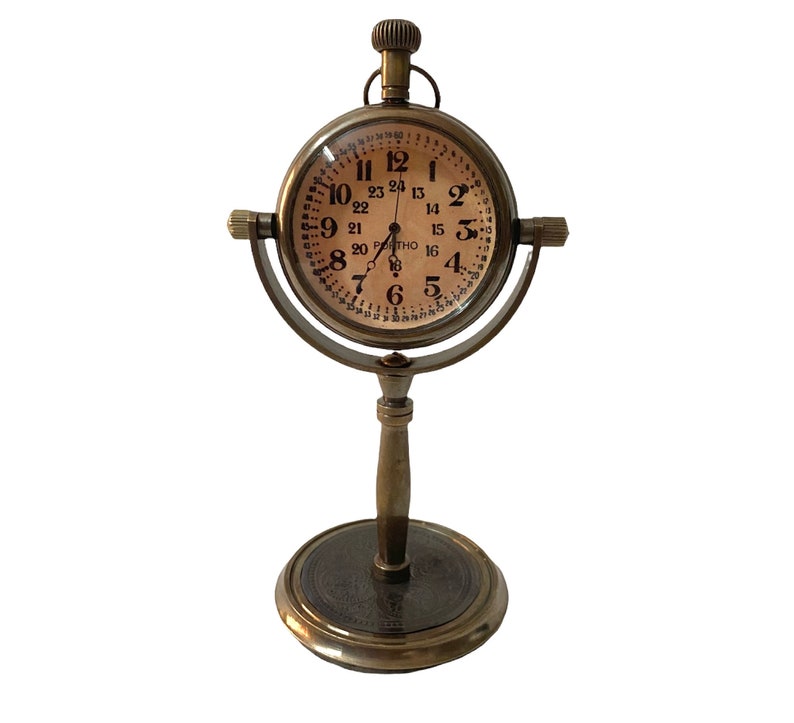 May include: A brass desk clock with a round face and a stand. The clock face has black Roman numerals and a 24-hour time scale.
