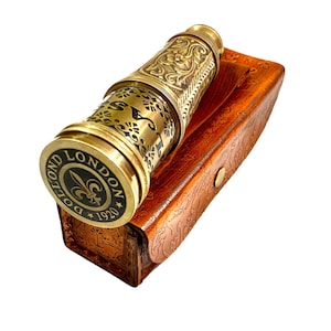 Può includere: Un telescopio in ottone con intricate incisioni floreali e a volute, appoggiato su una custodia in pelle marrone. Il tappo terminale del telescopio presenta la scritta "DOLLOND LONDON 1920" attorno a un emblema del giglio. La custodia ha una chiusura a bottone.