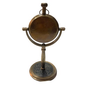 May include: A brass antique-style clock with a round face and a decorative stand. The clock has a black and gold design on the base.